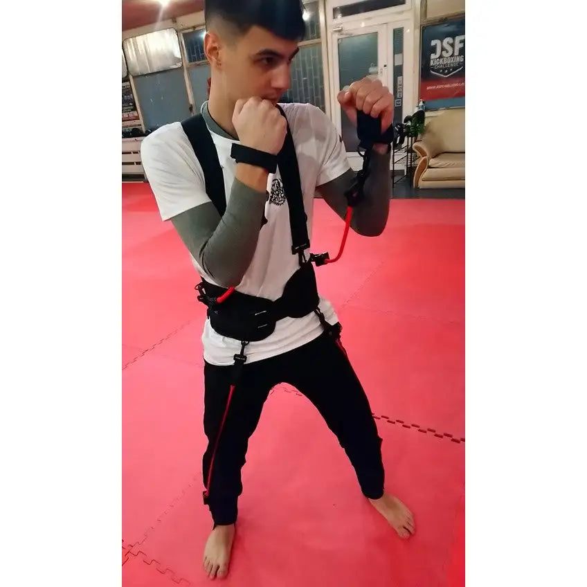 Boksetrening Kaugummi, person med svart sele og røde strikker i bokseposisjon på rød treningsmatte innendørs.