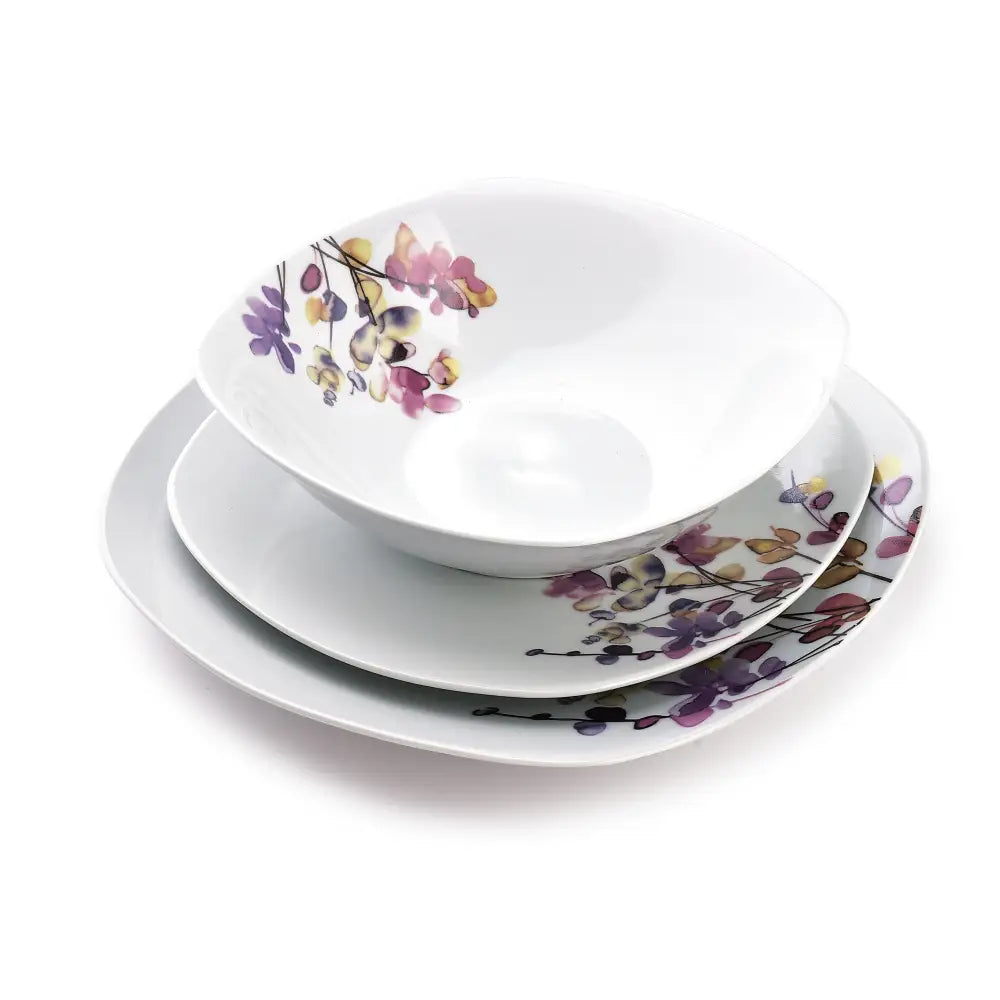 Botanisk lilla middagsservise, stablede hvite fat og bolle med blomsterdekor i lilla, rosa og gult.