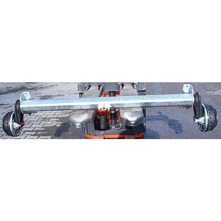 Aksling tilhenger AL-KO 1350kg, frontvisning av tverrbjelke med sorte hjul plassert på brosteinsunderlag.