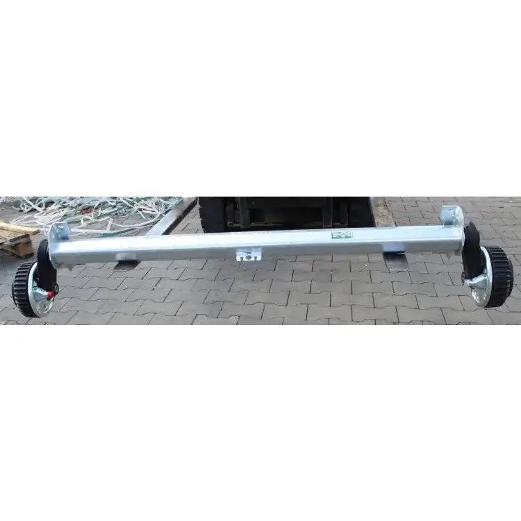 Aksling tilhenger AL-KO, sidevisning med svarte hjul i hver ende på steinlagt bakgrunn.