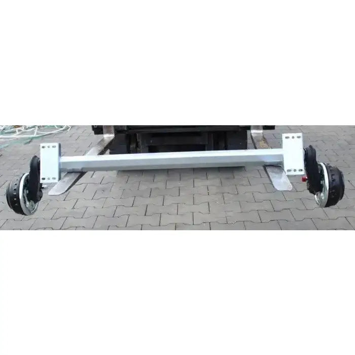 Aksling tilhenger AL-KO 1355mm, bakfra skrått, viser hjuloppheng og sølvfarget metall på brostein.