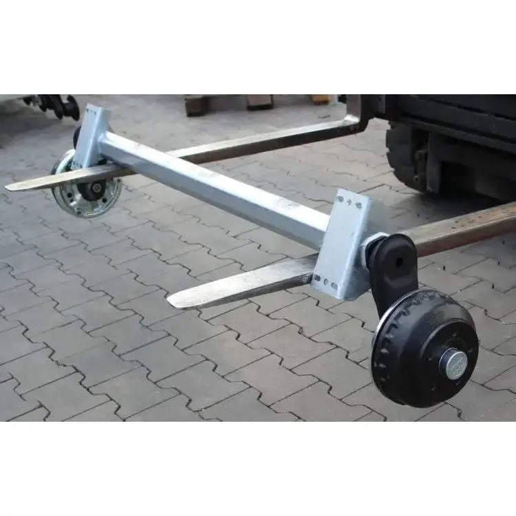 Aksling for tilhenger, sideperspektiv som viser hjuloppheng festet til truck på belegningsstein.