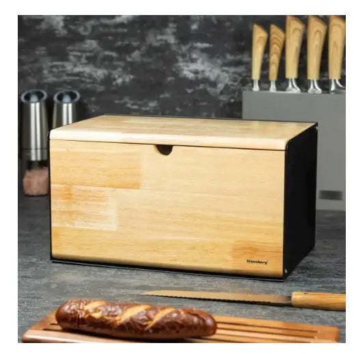 Brødboks i lyst tre med sorte sider, dobbel lokk, brødkniv og skjærebrett med brød foran på kjøkkenbenk.