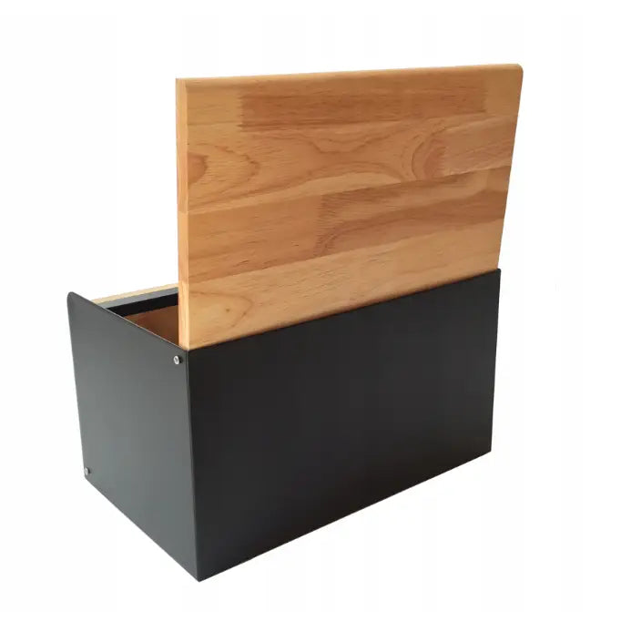 Brødboks i matt sort metall med lys trefarget skjærefjøl stående vertikalt, sett fra siden.