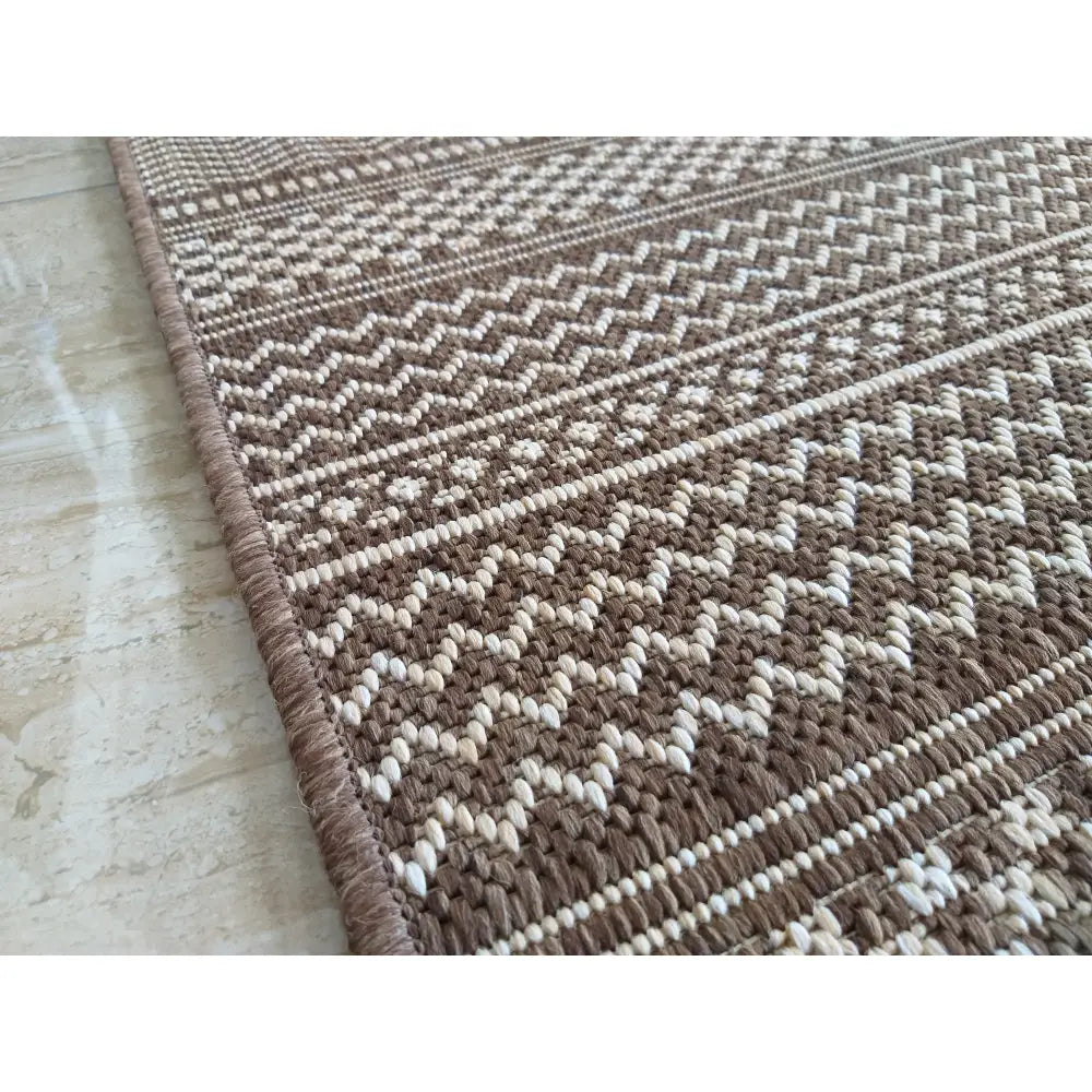 Brun Zara dobbelt-sidig tauteppet 200x290 cm, nærbilde av sikksakk- og stripemønster med forsterket kant.