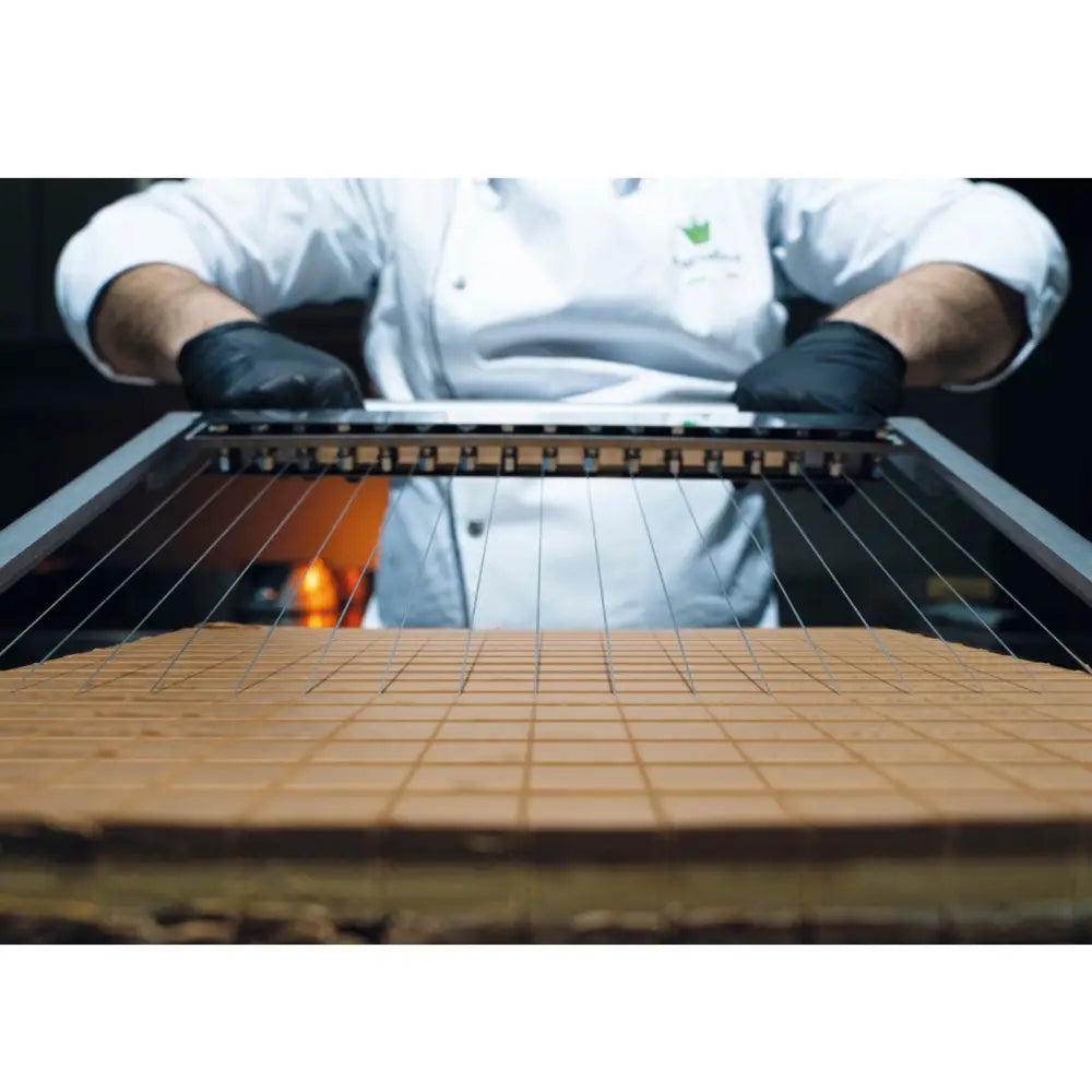 Cakery Guitar Dough Divider 3 Frame brukes av baker i hvit jakke og svarte hansker til å kutte konfekt i ruter.