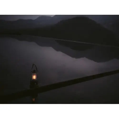 Campinglampe CAL 1 retro lyser ved vannkanten i skumring, omgitt av mørke fjell og rolig natur.