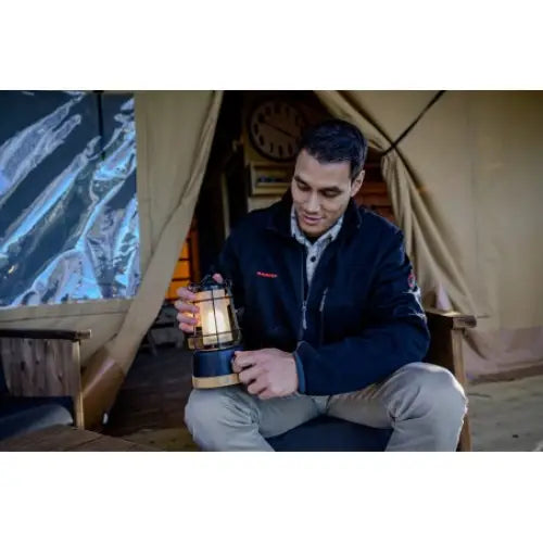 Campinglampe i retrostil holdes av mann foran telt, tent lykt i sort og messing med glasskuppel.