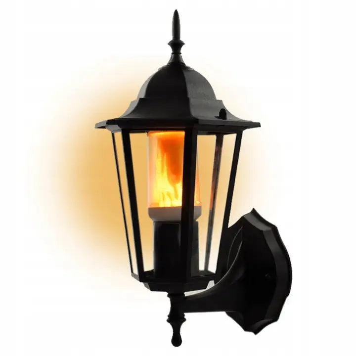 Dekorativ utendørs vegglampe i svart metall, sidevisning med tent oransje flammeeffekt bak glasspanelene.
