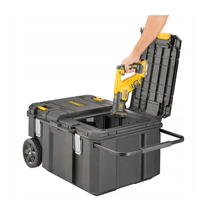 Dewalt Tstak koffert med åpnet lokk, hånd setter gult verktøy i kassen, hjul og håndtak synlige.