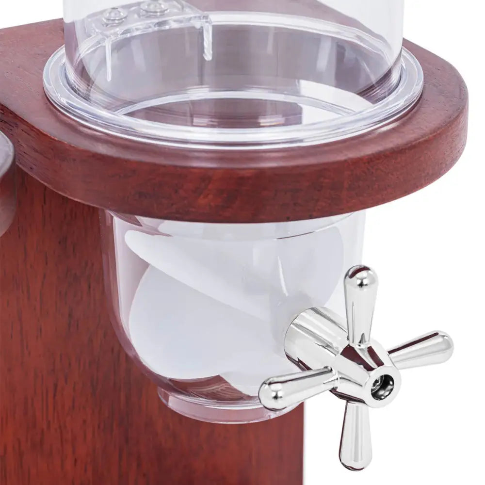 Dispenser for nøtter og søtsaker, nærbilde av klar beholder med hvit propell og sølv dreiekran på mørkt treverk.