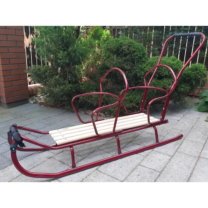 Dobbel tandem akebrett med rød metallramme, trebenk og høyt håndtak, sidevisning på uteplass.