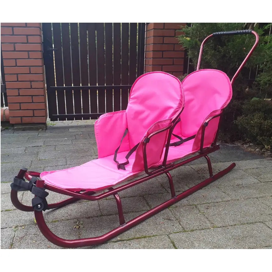 Dobbel tandem akebrett med rød metallramme, to rosa seter og belter, sett fra siden på uteplass.