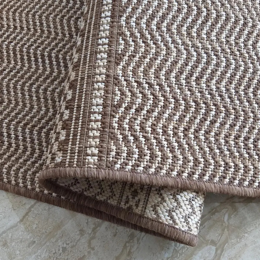 Dobbelt-sidig teppe Zara 12, nærbilde av beige og brun sikksakkstruktur med markert kant på lyst gulv.