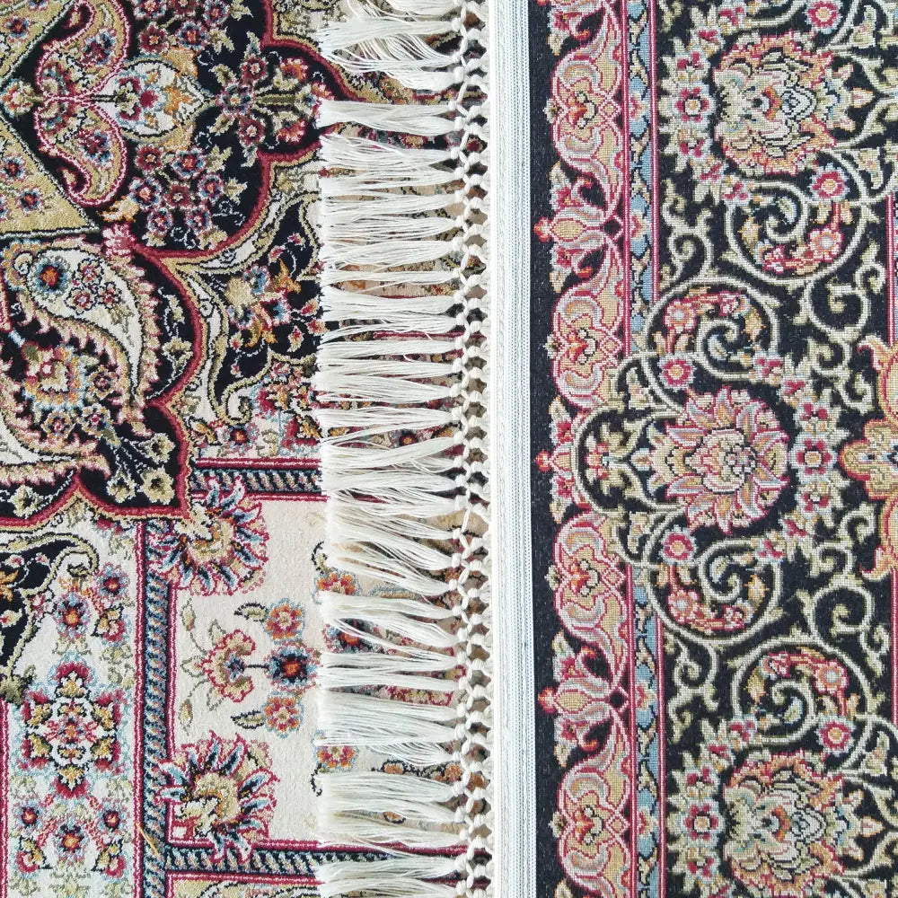 Eksklusivt kremfarget teppe med orientalsk mønster, frynsete kant og detaljerte blomstermotiver i flere farger.