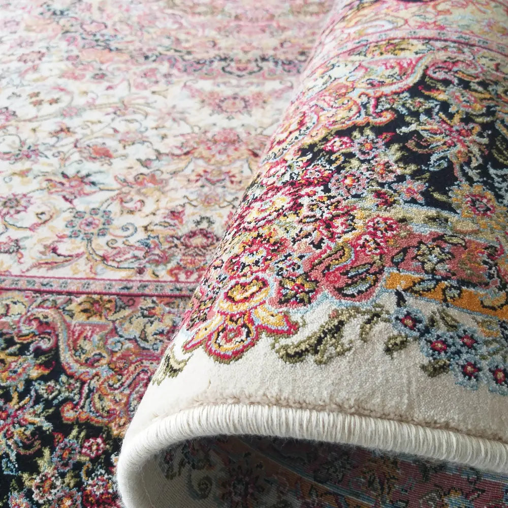 Eksklusivt kremet teppe 150 x 230 cm, sidevisning av delvis rullet ullteppe med fargerikt blomstermønster.