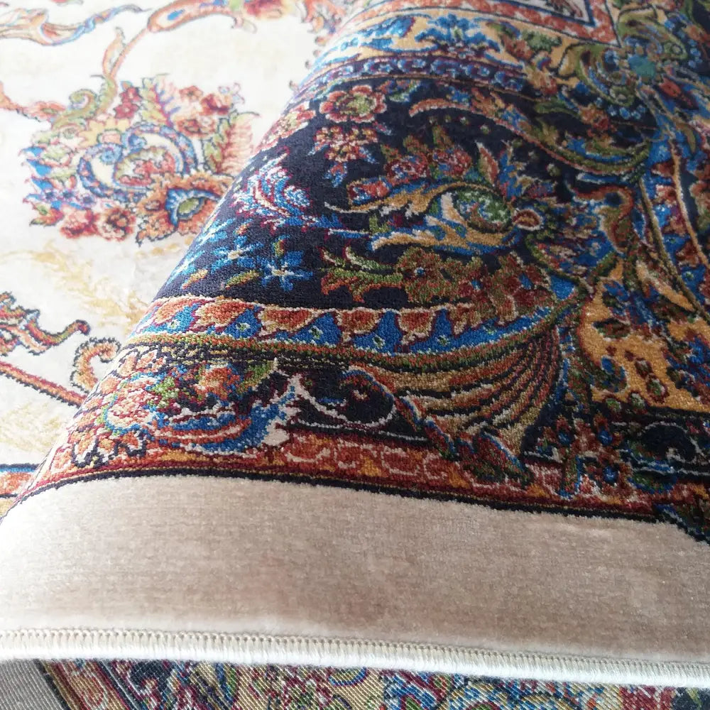 Qum Silk Tepe 08 krem teppe, nærbilde som fremhever det orientalske blå, røde og gylne mønsteret mot lys kant.
