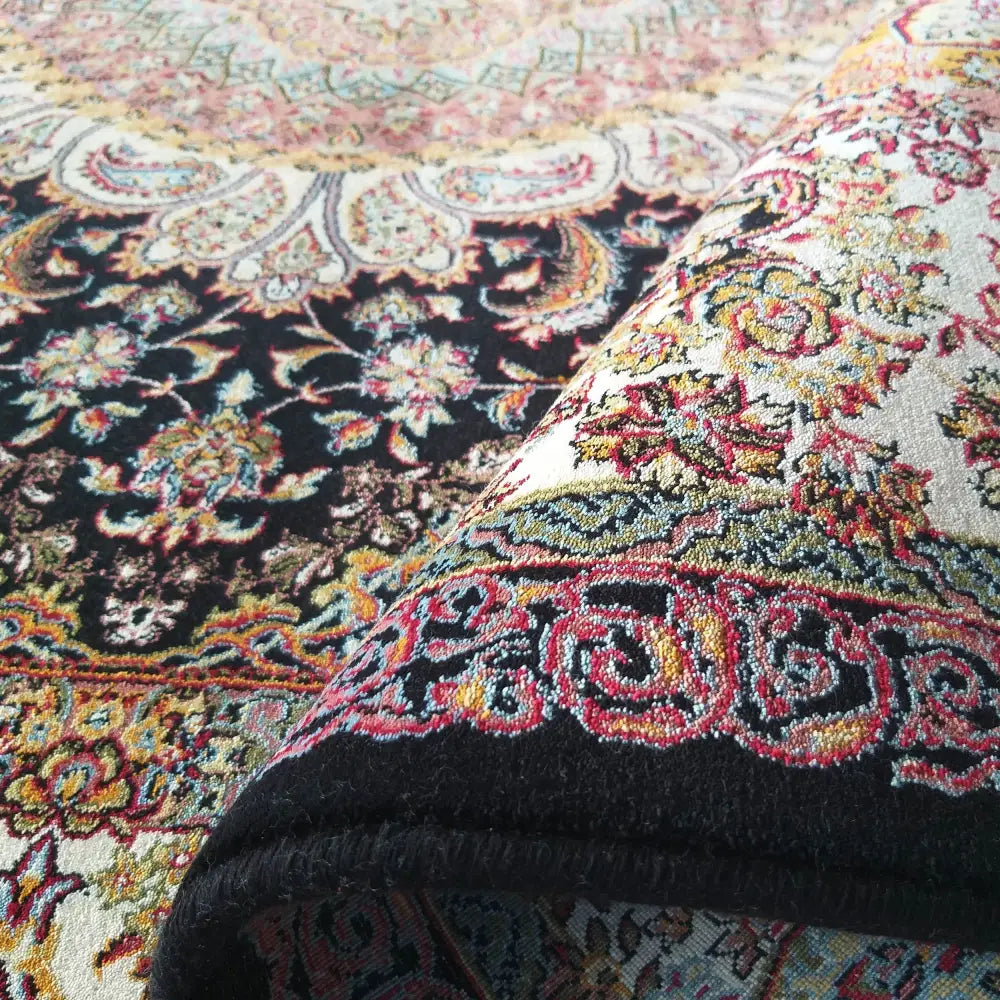 Orientalsk teppe i blått, svart, krem og rødt, detaljert blomstermønster, oppbrettet hjørne viser tykkelsen.