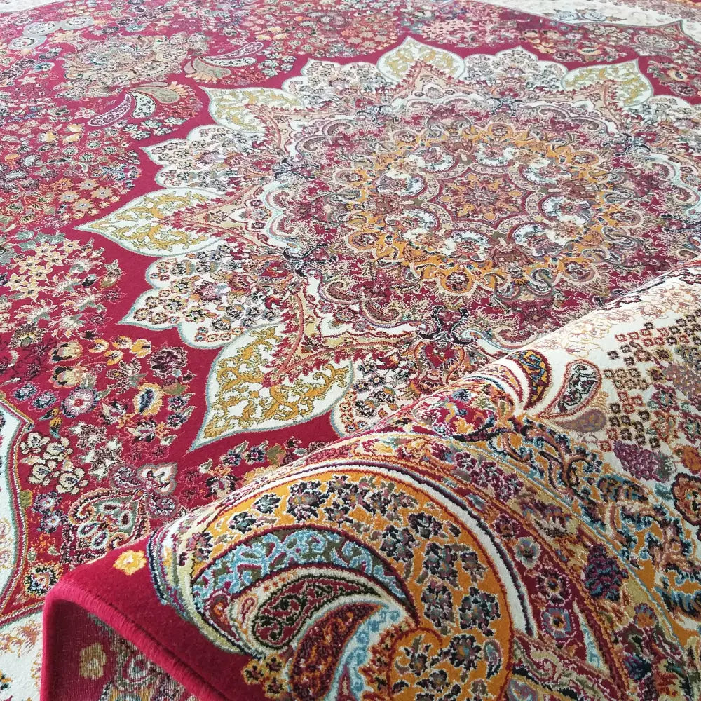 Eksklusivt orientalsk teppe i rødt med gule, hvite og blå blomster, nærbilde av brettet kant og detaljert mønster.