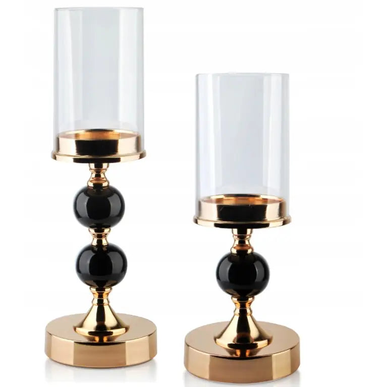 Elegant lysestake i gull og glass, sett fra siden, med sorte kuler og sylinderformet glasskuppel.