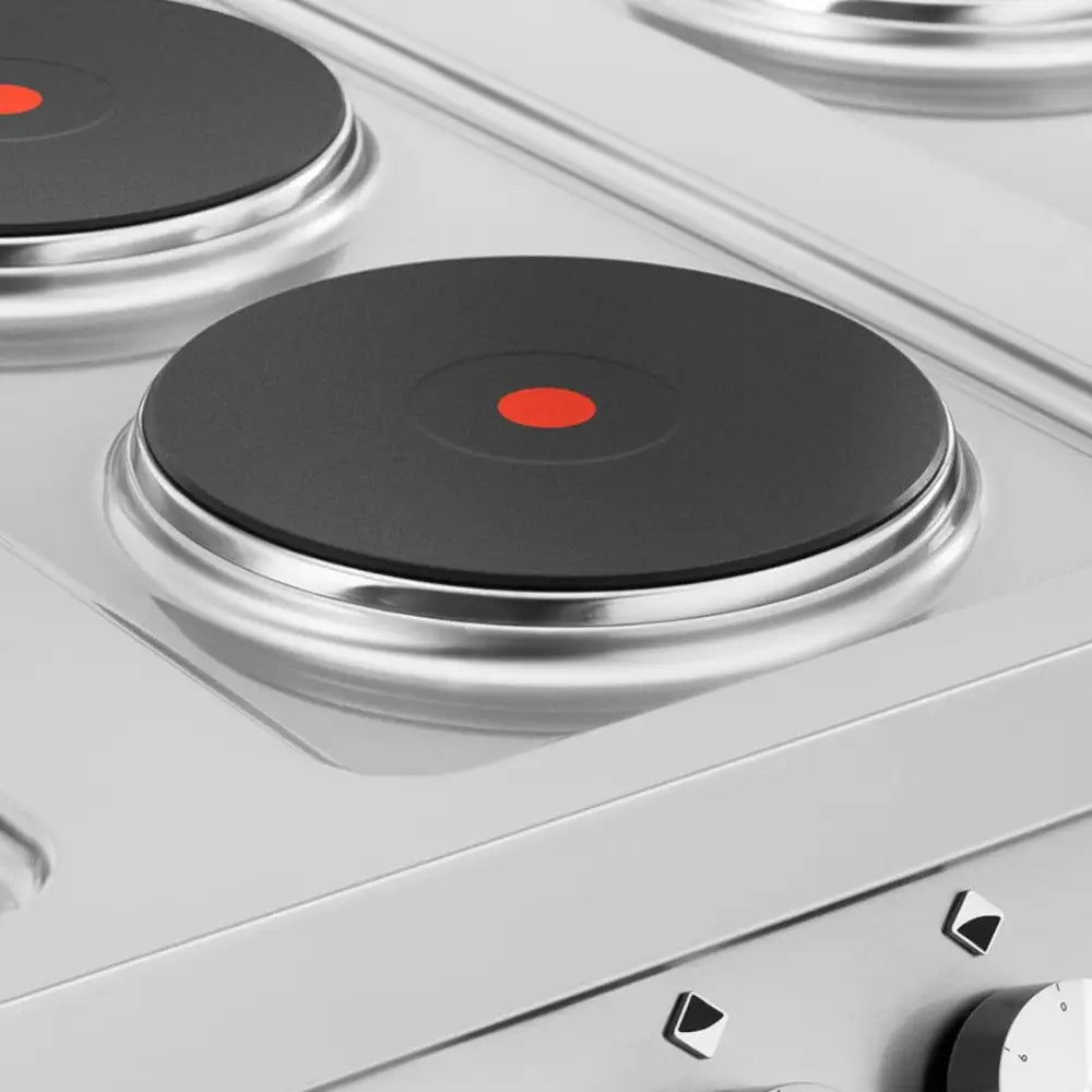 Elektrisk komfyr, nærbilde av svart støpejern kokeplate med rød indikatorprikk og plastknapper nederst til høyre.