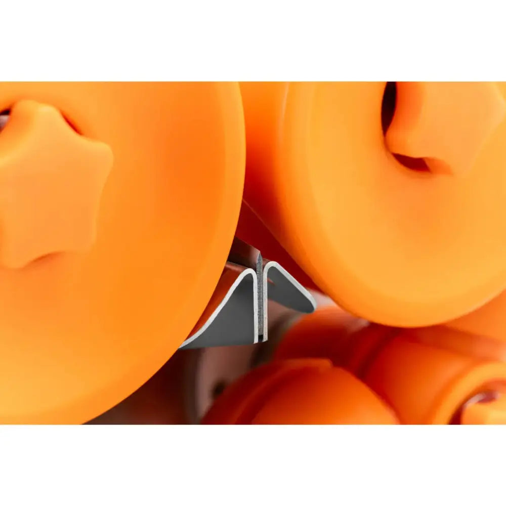 Elektrisk appelsinpress, detaljfokus på oransje plastdeksler med stjerneformede knotter og metallskinne mellom.