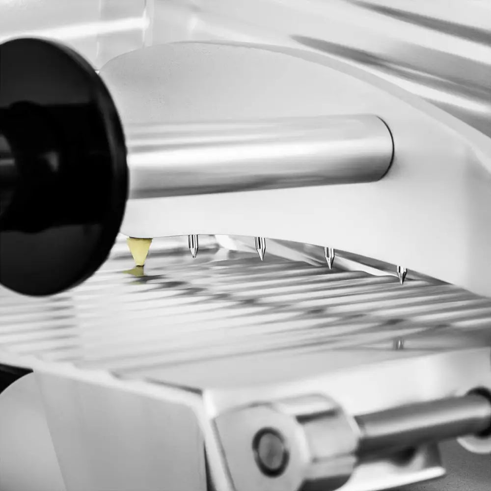 Elektrisk delikatesskiver, nærbilde av metallskive med riller, spisse tenner og sort håndtak fra siden.