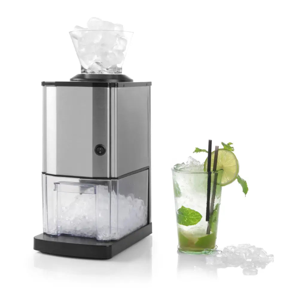 Elektrisk isknuser i rustfritt stål, fylt med isbiter, glass med drink, mynte og lime ved siden av.