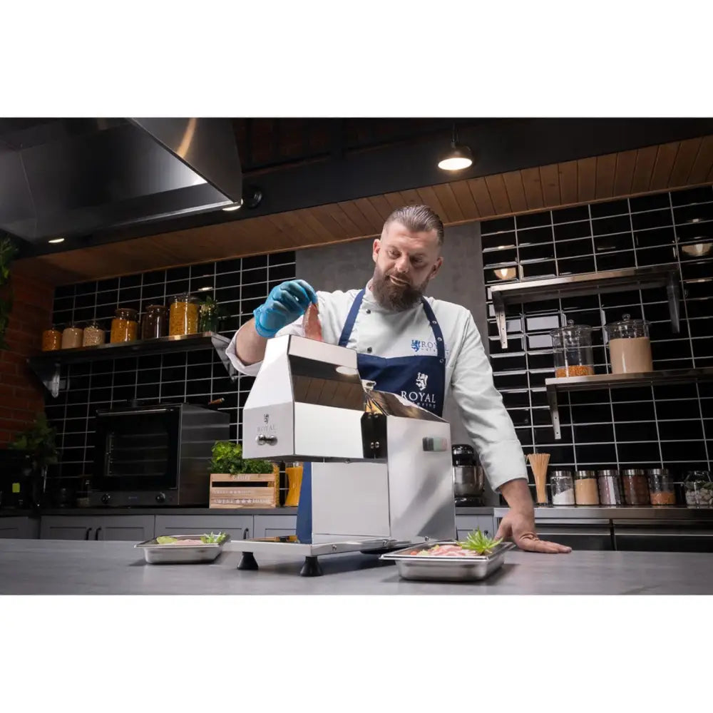 Elektrisk kjøttkvern Steaker maskin i bruk av kokk, sett skrått på kjøkkenbenk med serveringsfat foran.