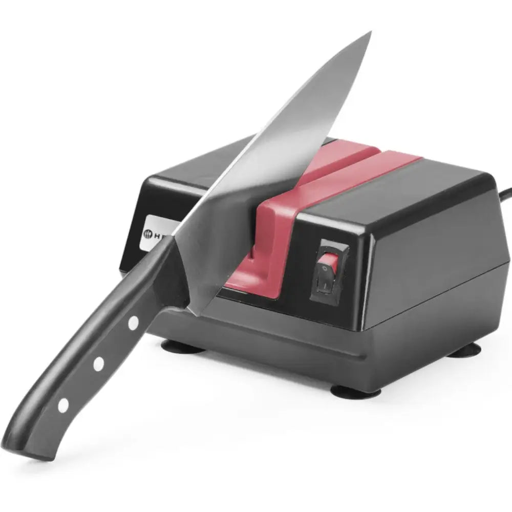 Elektrisk knivsliper i svart og rød plast, sett fra siden med kjøkkenkniv i slipemekanismen.