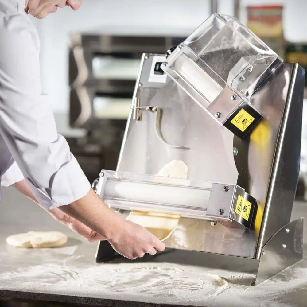 Elektrisk pizzadeig-kjevle i rustfritt stål, to ruller i bruk mens deig mates inn av en hånd.