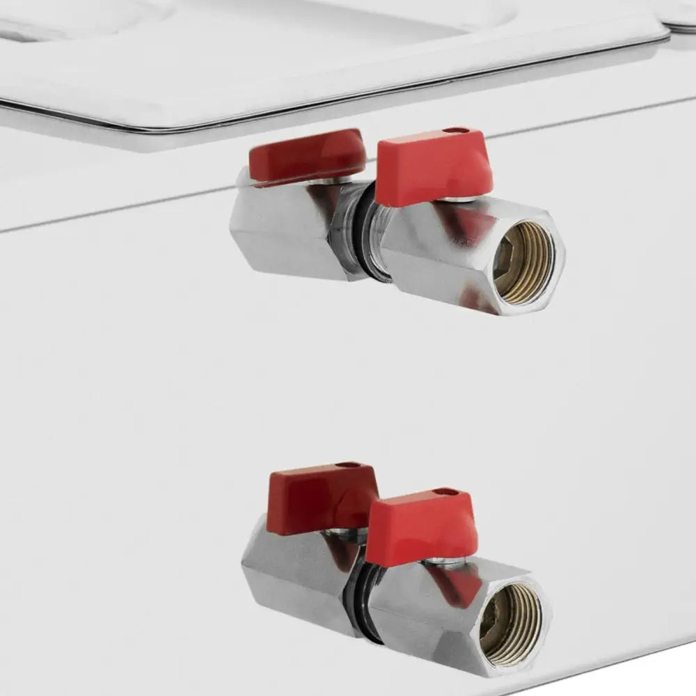 Elektrisk sjokoladesaus varmer, nærbilde av to metallventiler med røde håndtak på sølvfarget overflate.