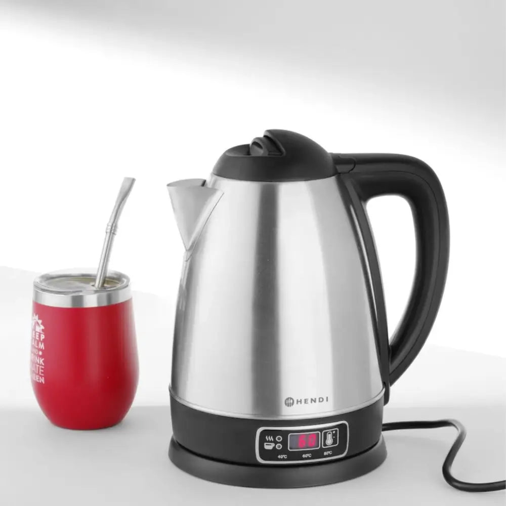 Elektrisk trådløs vannkoker i rustfritt stål, sidevisning med digitalt display, svart håndtak og rød kopp ved siden av.
