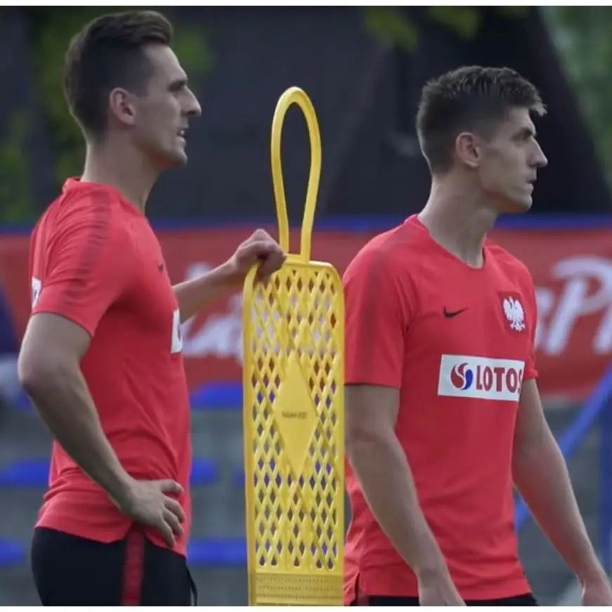 Elite Fotballmål 180 cm blå, to menn i rødt trener utendørs ved gul plastfigur på fotballbane.