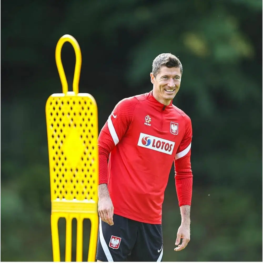 Elite Fotballmål 180 cm Blå, utendørs treningsøkt med gul plastfigur på gressbane ved siden av mann i rød genser.