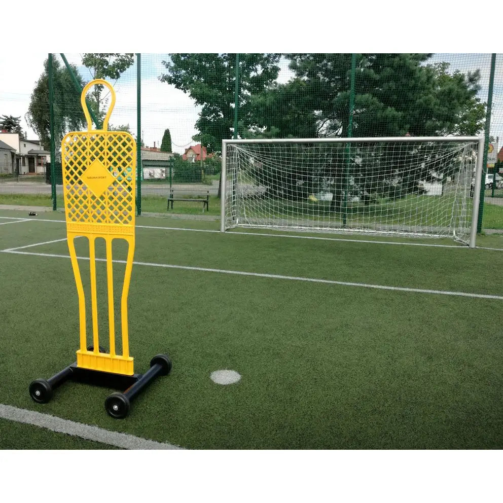 Elite fotballmurmester vogn med gul treningsfigur på hjul, sett skrått foran fotballmål på gress.