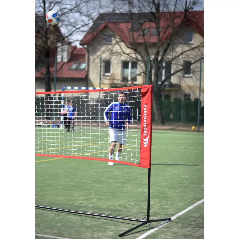 Elite Pro Indoor Volleyball Net Set på kunstgress, nett med svart ramme og rød kant, person i blått bak nettet.