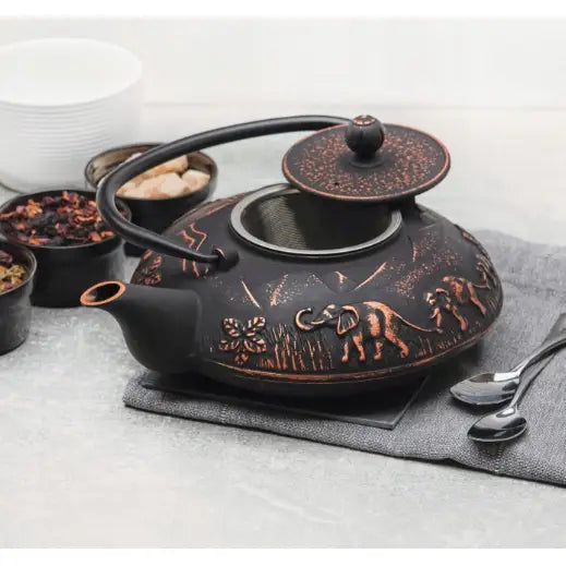 Sort emaljert støpejernstekanne med kobberdetaljer og elefantmotiv, åpent lokk og synlig infuser.