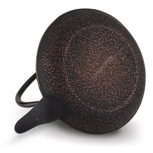 Non-stick stekepanne sett ovenfra med mørk overflate, rødbrune prikker og synlig inngravert logo på bunnen.