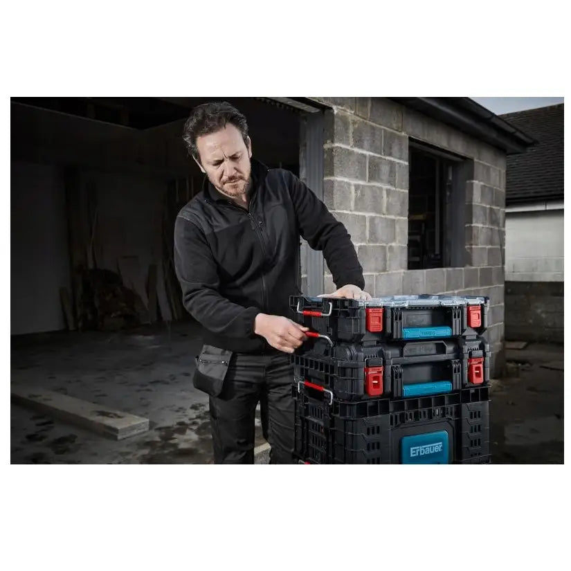 Erbauer Connecx stablebar verktøykasse i bruk utendørs, skrå vinkel, røde og blå detaljer mot murvegg.