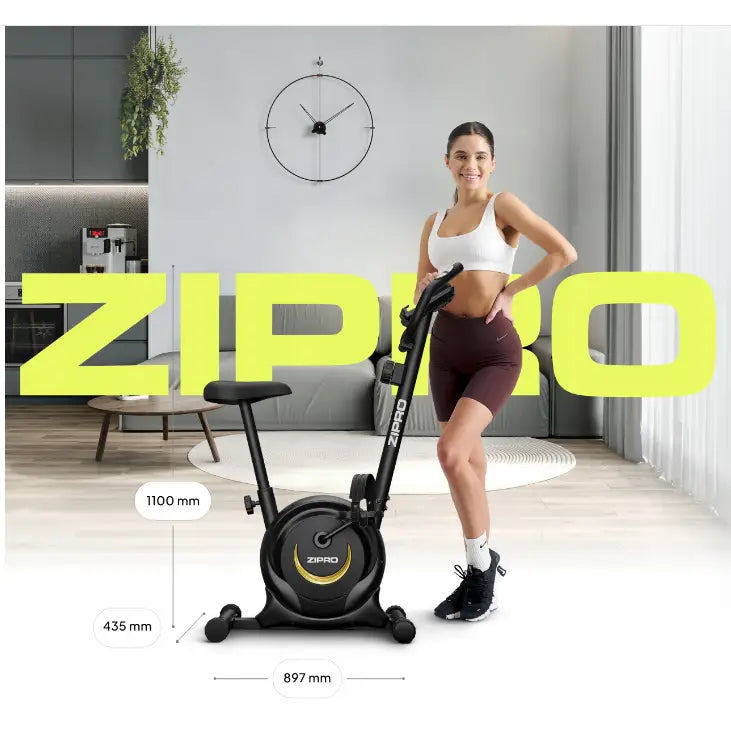 Ergometersykkel Zipro One i sort med gule detaljer, sidevisning ved smilende kvinne, mål oppgitt i moderne stue.
