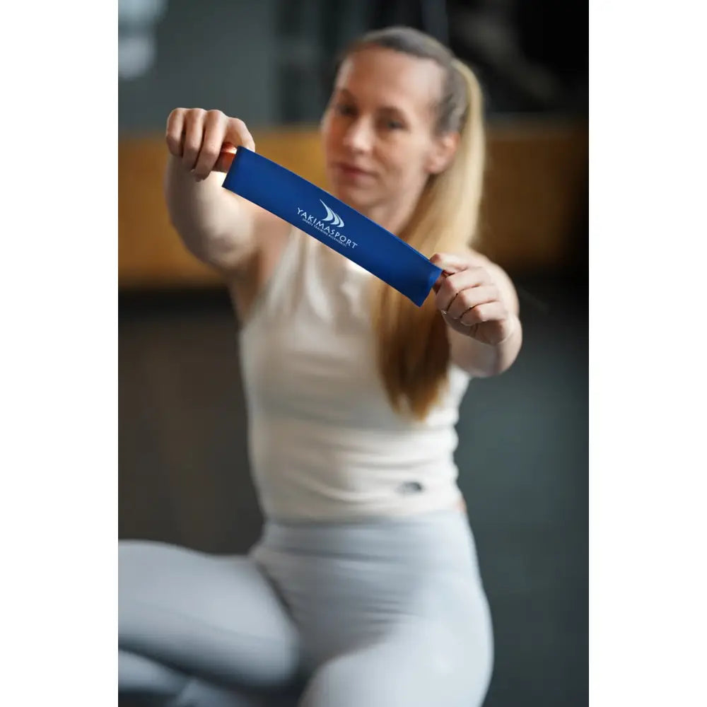 Blå treningsstrikk med stor motstand, strukket mellom hendene til kvinne i treningstøy, nærbilde.