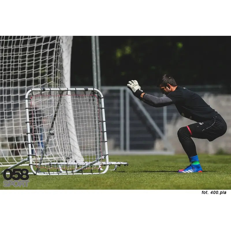 Fjærbrett med nett sett fra siden på gressbane, målvakt i sort utstyr gjør seg klar foran rebounderen.