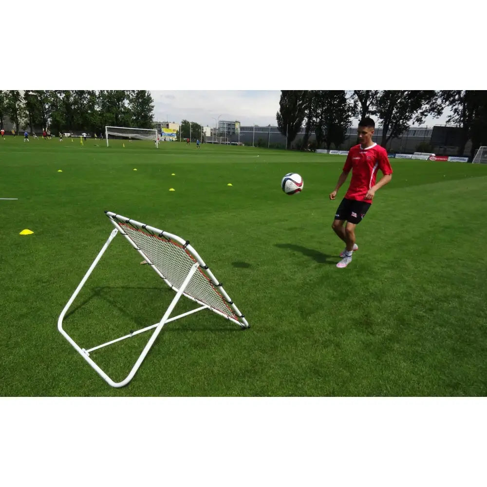 Fjærbrett med nett, skråvisning i bruk på gressbane med fotball og treningskjegler rundt.