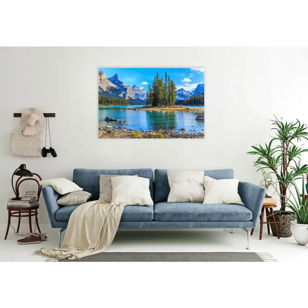 Fjell og innsjø lerretsbilde over blå sofa, omgitt av grønne planter og lyse puter i moderne stue.