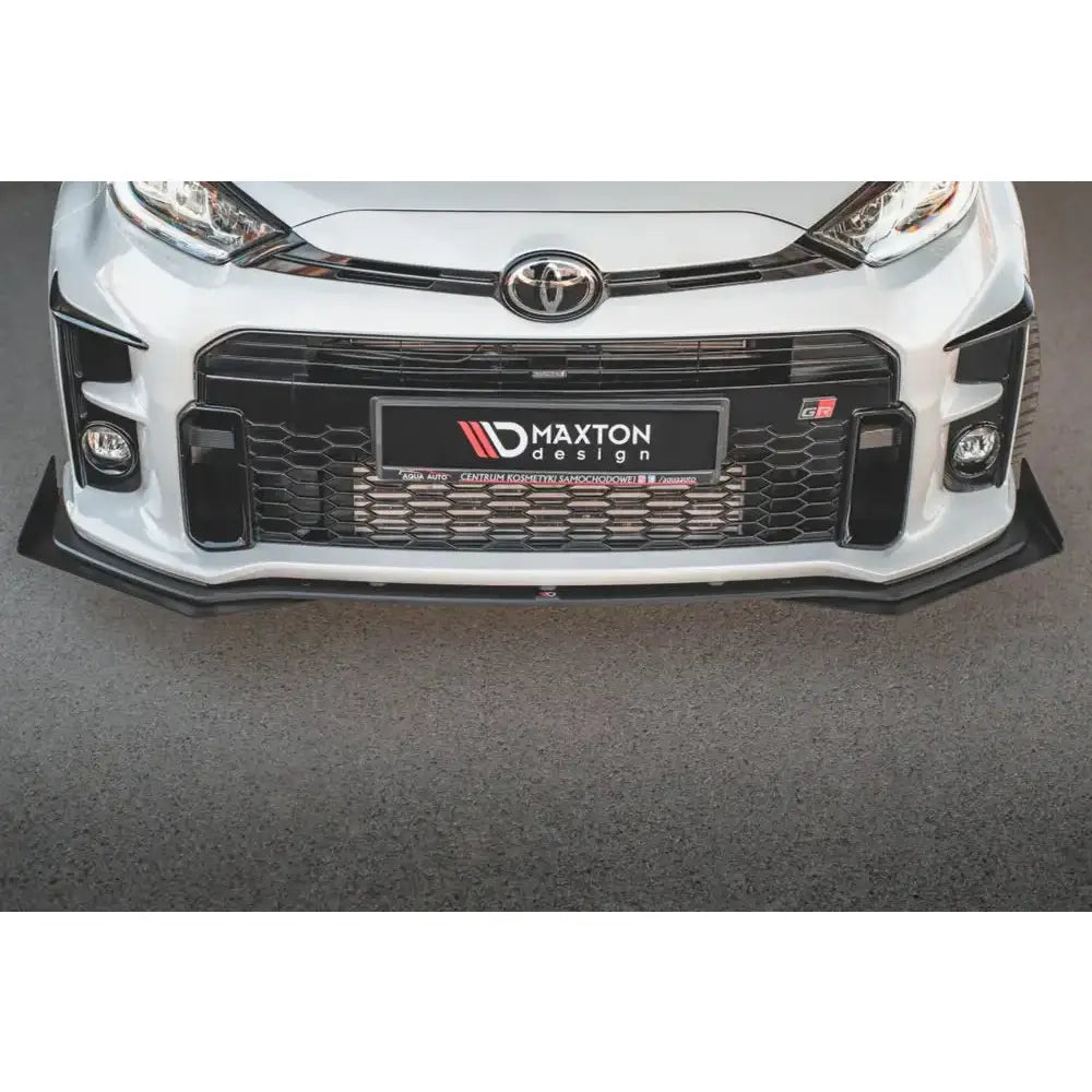 Frontleppe til Toyota GR Yaris Mk4 i sort plast montert foran på hvit bil, sett forfra mot asfalt.