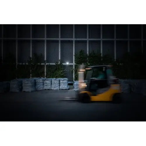 Gul gaffeltruck kjører forbi plastinnpakkede varer i dempet lagerbelysning, sett fra siden.