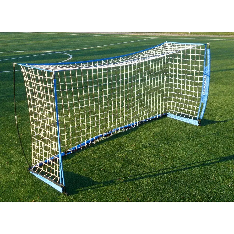 Foldbart fotballmål UNI ŻAK, hvit netting og blå ramme, skrå forfra på grønn kunstgressbane.
