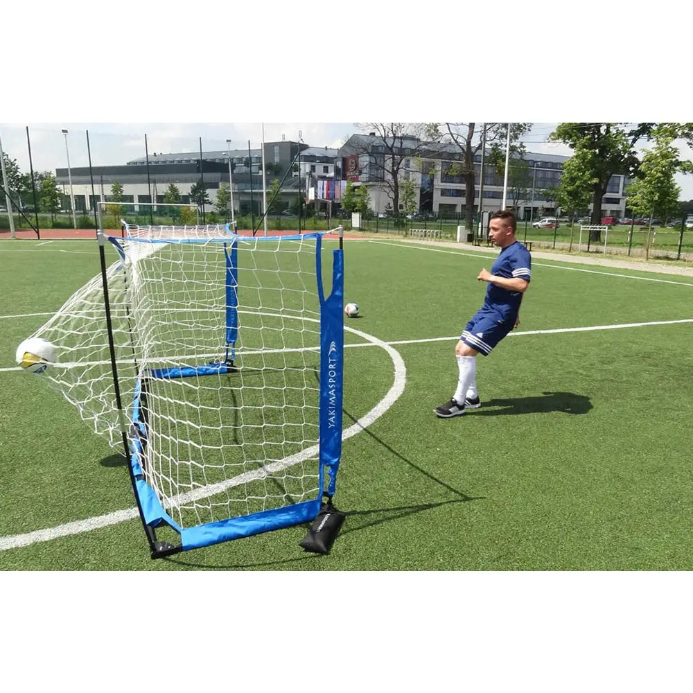 Foldbart fotballmål UNI ŻAK på kunstgress, ball treffer nett mens spiller i blått følger etter fra siden.