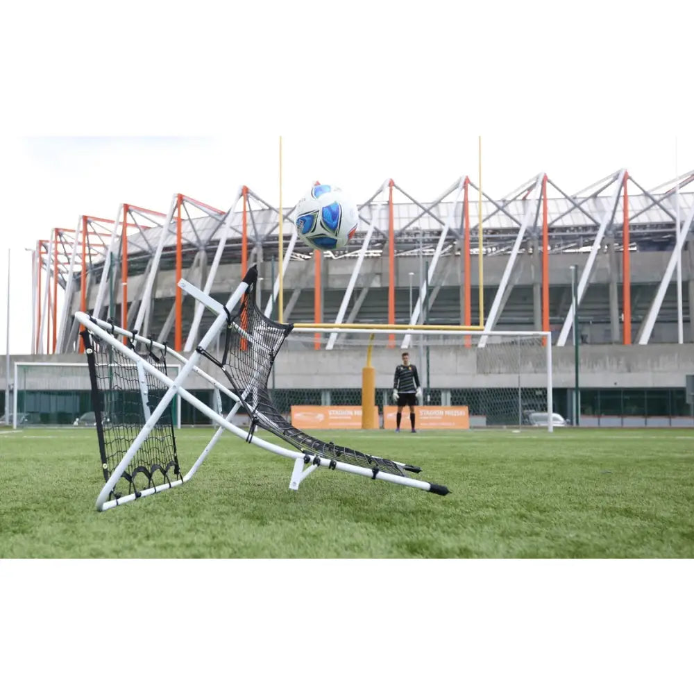 Fotball rebounder med hvit ramme og svart nett, sidevisning mens ballen spretter tilbake på kunstgress.